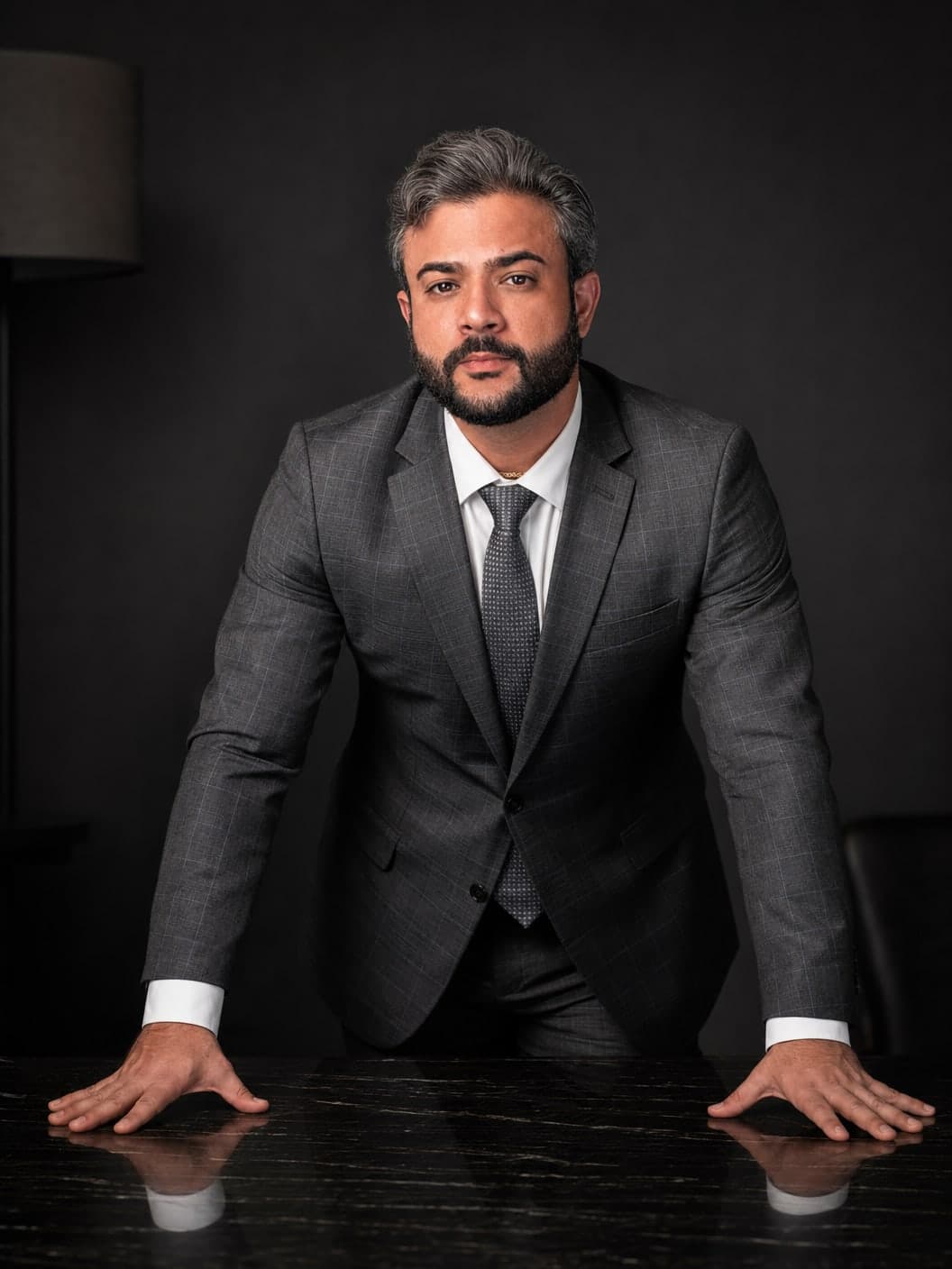Rafael Estrella, advogado, de terno cinza, com as mãos apoiadas sobre uma mesa escura